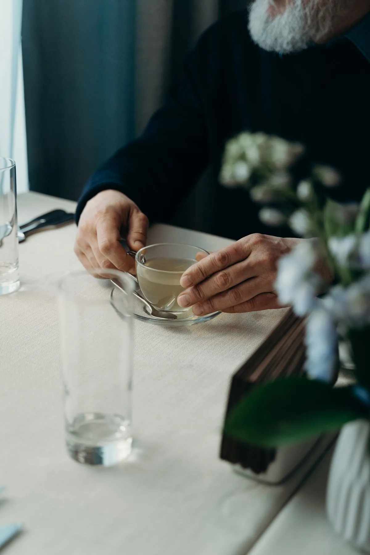 Hände halten eine Tasse Tee an einem gedeckten Tisch